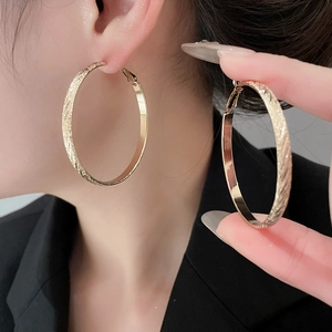 Detailed close-up of large golden textured hoop earrings worn on a model's ear