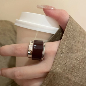 Detail of a wide silver band ring with deep red enamel worn while holding a coffee cup