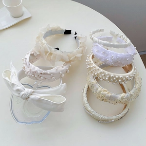 Close-up of white oversized bow and pearl headbands in elegant cream fabric