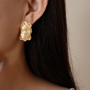 Close-up of golden irregular textured stud earrings shown on a model's ear