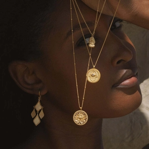 Détail de colliers Hamsa plaqués or 18 carats superposés sur un mannequin à peau foncée