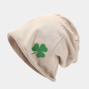Dettaglio del berretto in maglia beige con logo a trifoglio verde e bordo arrotolato