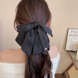 Macro view of a large black satin bow hair claw with a small gold logo on the back of a model