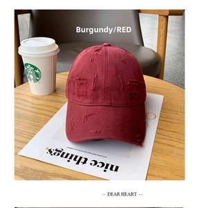 Close-up of wine red distressed baseball cap with ripped details and cotton texture