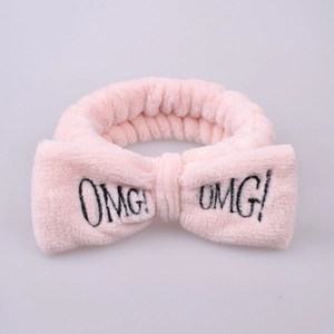 Close-up of pink plush headband featuring a large bow and black OMG embroidery detail