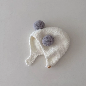 Close-up of white plush baby earflap hat with grey pom-poms and wooden button details