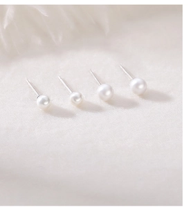Macro shot of four white shell pearl earrings with silver pins in various sizes