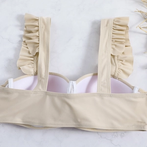 Detail of beige ruffled bikini top with padded cups on white marble background