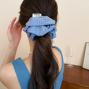 Detailed view of blue and white checkered fabric scrunchie worn on a high ponytail
