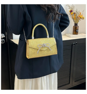 Gros plan d'un sac carré à paillettes dorées avec papillon en strass et chaîne métal