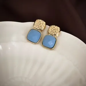 Detail of geometric blue square stud earrings with golden hammered metal on a white bowl