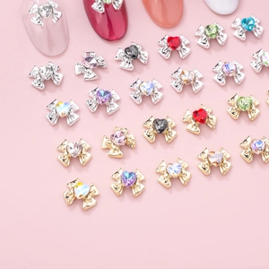 Detailed view of colorful heart crystal bow nail charms on a soft pink surface