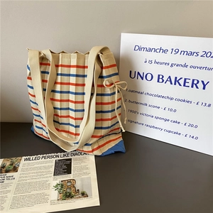Striped knitted tote bag with blue and red patterns and side drawstrings in a minimalist setting
