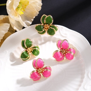 Detailansicht der floralen Emaille-Ohrstecker in Grün und Rosa auf einem Porzellanteller