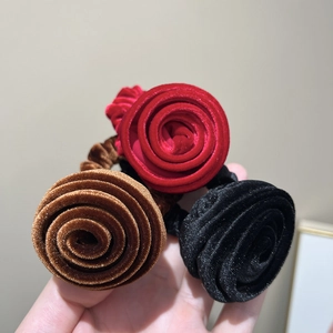 Trois chouchous roses en velours rouge, marron et noir, présentés dans une vue de main proche