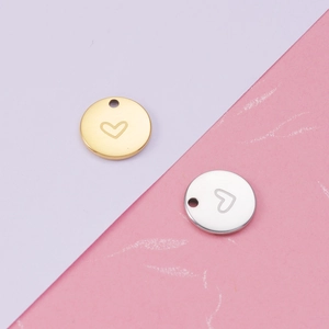 Close-up of gold and silver heart-engraved round pendants on white and pink textured background