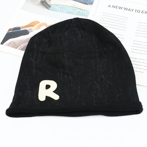 Détail d'un bonnet en maille noire avec bord roulé et écusson lettre R blanc sur fond plat