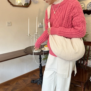 Detail of a large beige crescent crossbody bag paired with a rose pink knit sweater