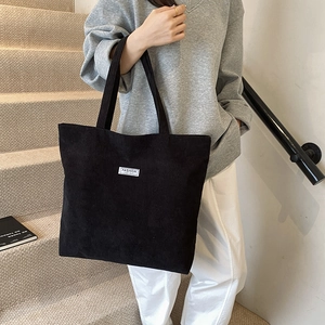Detailed view of large black corduroy tote bag worn by model on minimalist stairs