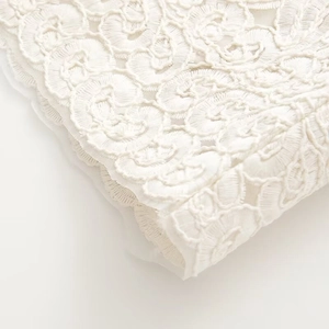 Close-up of intricate white lace embroidery texture on a hollow-out casual shirt
