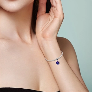 Détail d'un bracelet maille serpent argenté avec un pendentif flocon bleu sur un poignet