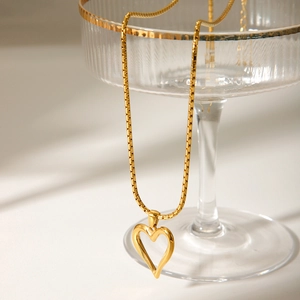 Close-up of golden hollow heart pendant necklace hanging on a crystal glass rim