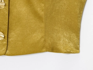 Dettaglio del tessuto satinato giallo zenzero con bottoni metallici dorati irregolari