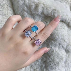 Detailed view of three emerald-cut gemstone rings on fingers with white faux fur background