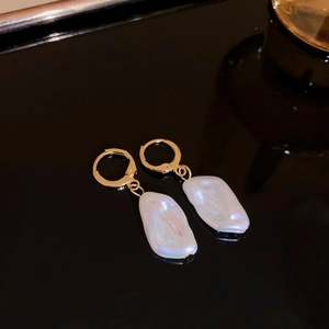 Close-up of gold hoop earrings with white baroque pearls on a sleek black background