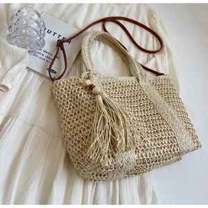 Detail of beige straw tote bag featuring woven texture and decorative wooden bead tassels