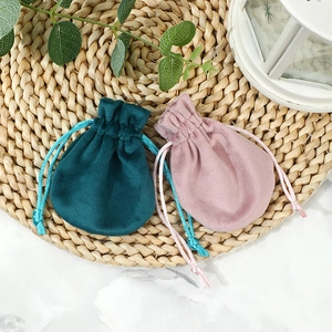 Thick velvet jewelry pouches in green and pink with drawstring closures on marble surface
