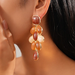 Macro shot of amber resin oval drop earrings with gold metal edges worn by a model