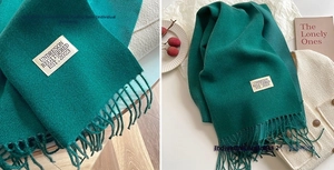 Detail of dark green cashmere-feel scarf with long tassels and branded woven label