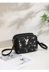 Detailed close-up of pink floral and butterfly embroidery on a black faux leather camera bag