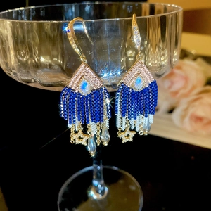Detailed shot of sparkling star and water drop crystal tassel earrings on glass rim