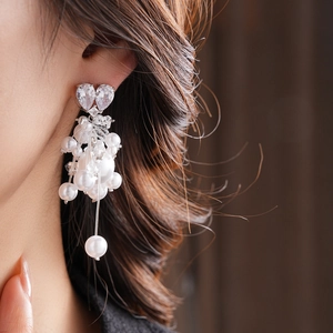 Close-up of elegant long pearl tassel earrings with heart-shaped zircon on a model
