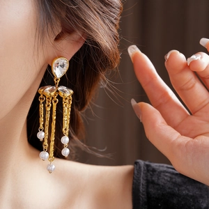 Close-up of gold tassel earrings with teardrop crystal and white pearl droplets