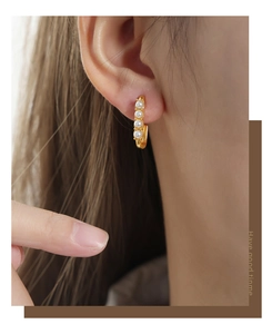 Detail view of gold hoop earring with four white pearls on a model's ear