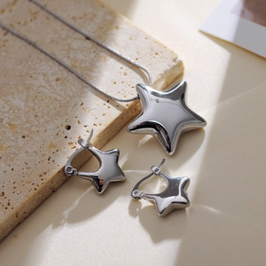 Polished silver star pendant necklace and matching star hoop earrings on a stone surface