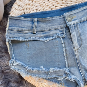 Dettaglio degli shorts in denim a vita alta con bottone e design della tasca anteriore