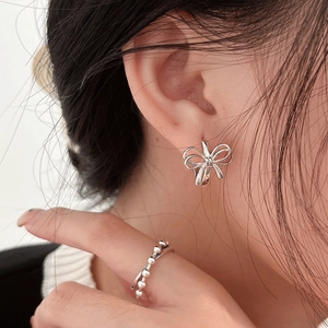 Detailed close-up of a silver bow earring and beaded ring worn by a fashion model
