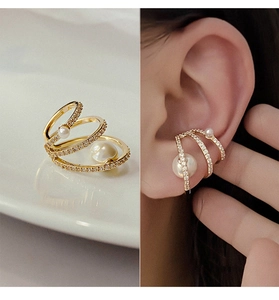 Close-up of gold ear cuff with white pearls and diamonds next to a model's ear