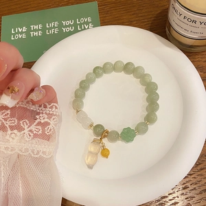 Detail view of jade bead bracelet featuring a translucent peanut pendant and floral charm