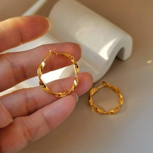 Eleganti orecchini a cerchio intrecciati dorati in argento S925 tenuti da una mano su base