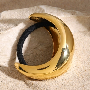 Close-up of a crescent-shaped gold metal hair tie placed on beach sand and rock