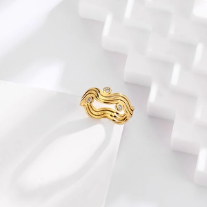 Macro shot of wavy gold ring with cubic zirconia stones on a white geometric block