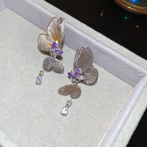 Macro detail of silver butterfly earrings with purple crystal droplets on gray velvet