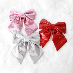 Three sequined Christmas bows in red pink and silver on a white snowy background