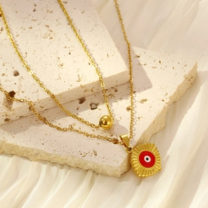 Detail of gold double-layered necklace with bead and red devil eye square pendant
