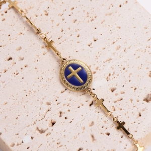 Golden stainless steel chain bracelet with blue enamel cross charms on stone background